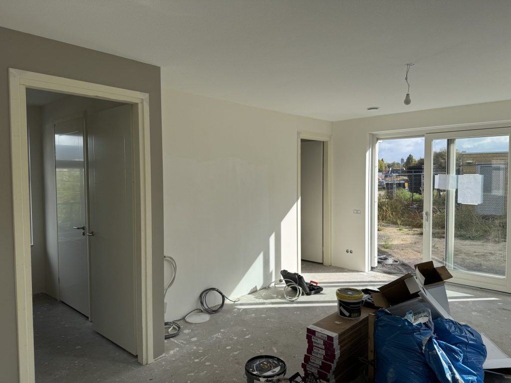 Woonkamer tijdens de afwerking, met verfemmers en materiaal op de vloer