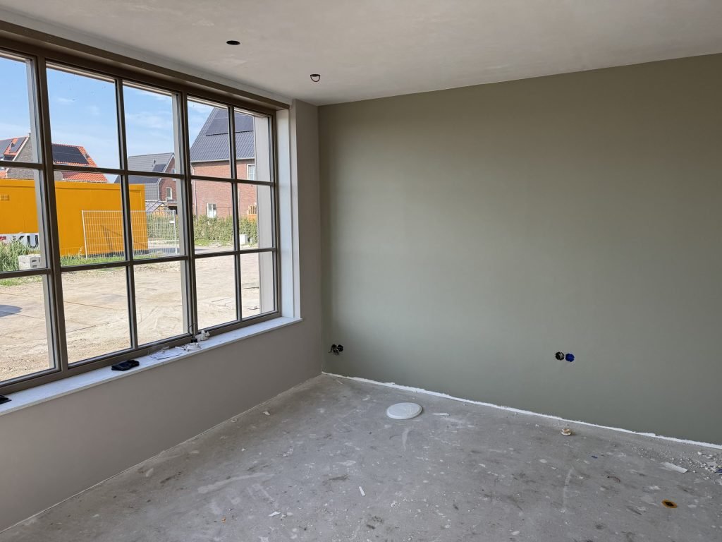 Wand in een grijsgroene tint naast een grote raampartij in een lege kamer