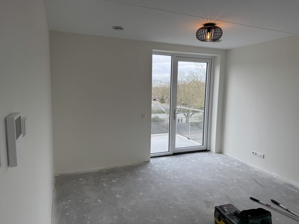 Lege kamer met strakke witte wanden en openslaande deuren naar het balkon