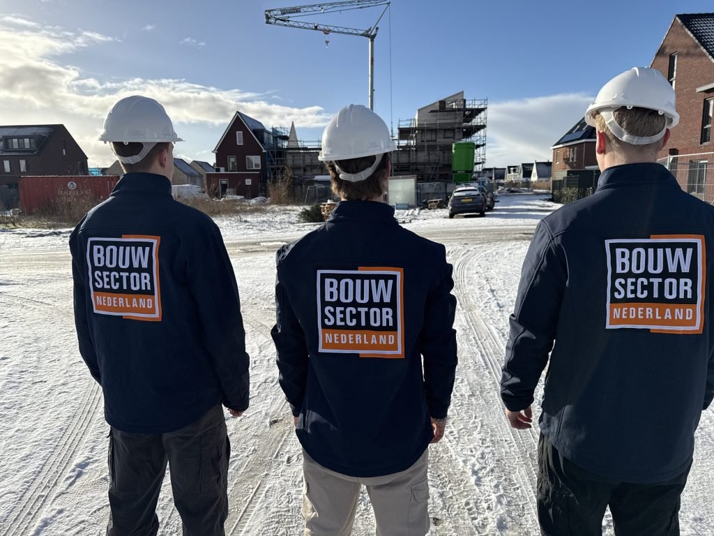 Drie vakmensen van Bouwsector Nederland met witte helm en logo op de rug bij woningen in aanbouw